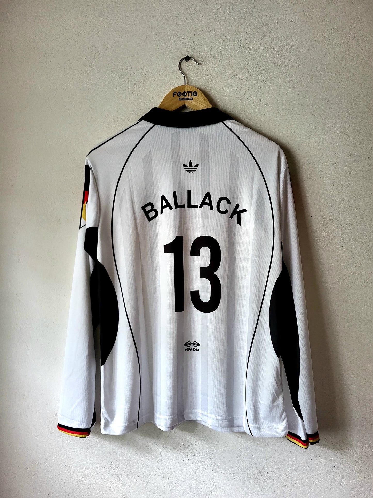 A white long-sleeve Germany national team soccer jersey with 'BALLACK 13' printed on the back, hanging on a wooden hanger against a textured off-white wall.