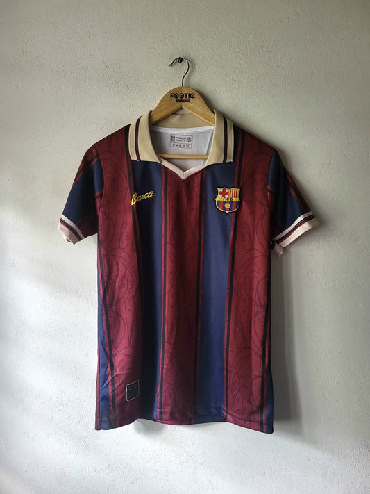 A vintage FC Barcelona soccer jersey by Kappa, featuring the iconic maroon and navy blue vertical stripes with cream accents on the collar and sleeve cuffs, hanging on a wooden hanger against a textured off-white wall.