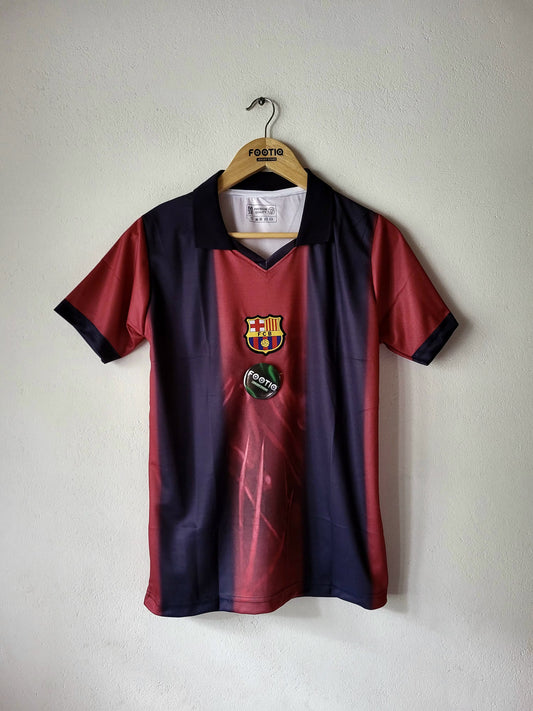 A vintage FC Barcelona soccer jersey hanging on a wooden hanger against a plain off-white wall. The jersey features a vertical color-blocked design with dark navy blue on the top half, a red-to-purple gradient in the middle, and dark navy on the bottom half.