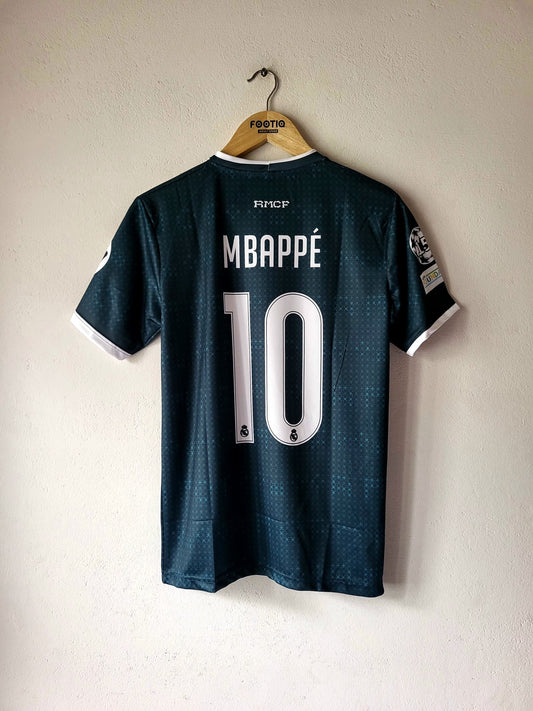 A dark teal Real Madrid soccer jersey with 'MBAPPÉ 10' printed on the back, hanging on a wooden hanger against a textured off-white wall.