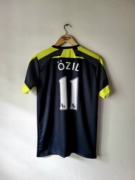 A dark navy blue soccer jersey with neon yellow-green accents on the shoulders and sleeves, featuring the name 'ÖZIL' and number '11' on the back. The jersey is hanging on a wooden hanger with 'FOOTBALL' printed on it, against a plain light gray wall.