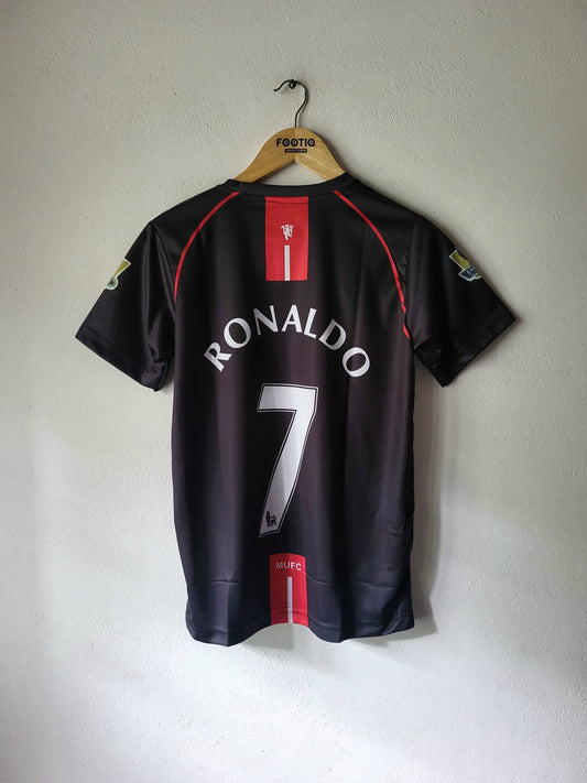 A black Manchester united soccer jersey with 'RONALDO 7' printed on the back, hanging on a wooden hanger against a light gray wall.