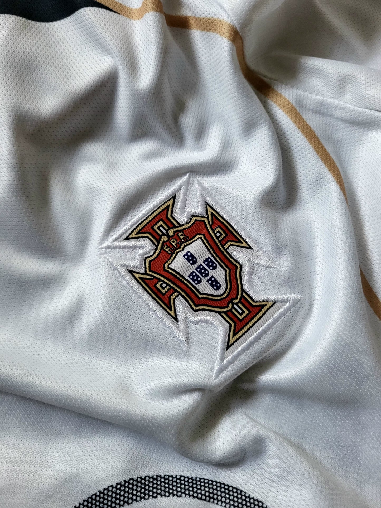 Close-up of a white Portugal soccer jersey fabric showing the embroidered national team crest on the chest.