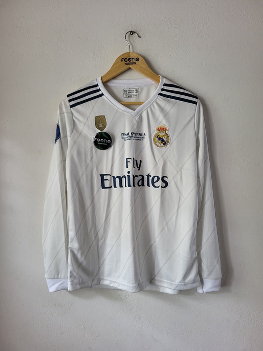A white Real Madrid long-sleeve soccer jersey with 'Fly Emirates' sponsor text, hanging on a wooden hanger against a plain wall.