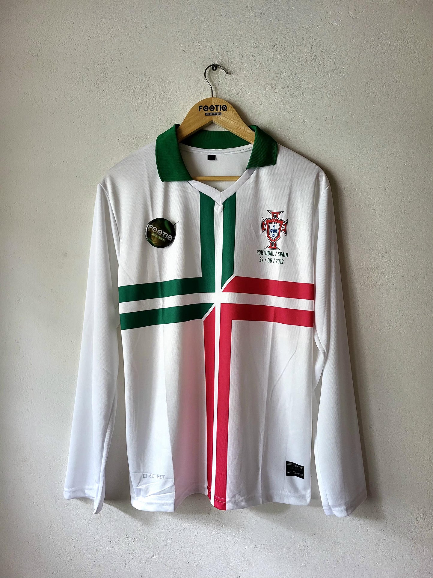 A white Portugal national football team long-sleeve jersey with green and red vertical stripes, hanging on a wooden hanger against a textured beige wall.