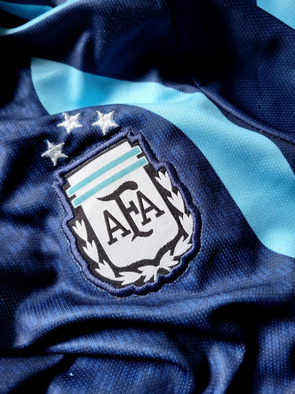 Close-up of a dark blue textured sports jersey with a light blue diagonal stripe and the embroidered Argentina Football Association (AFA) crest featuring three stars.