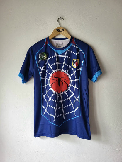 A blue short-sleeve Atletico Madrid soccer jersey with a Spider-Man web and red spider graphic on the front, hanging on a wooden hanger against a plain wall.