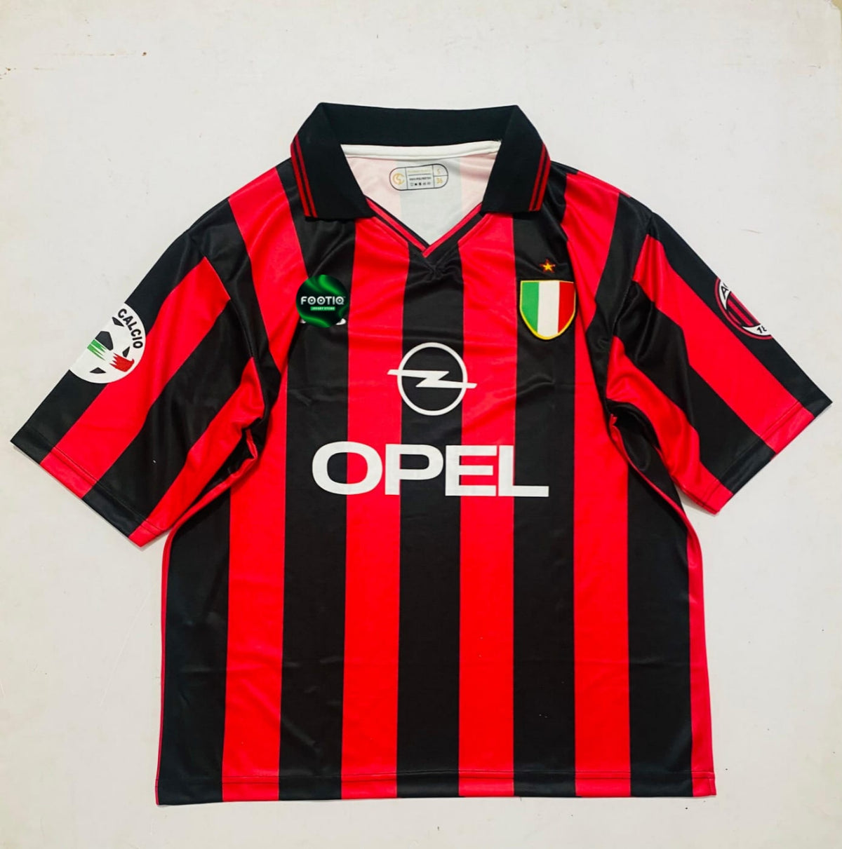 A vintage AC Milan soccer jersey with red and black vertical stripes, featuring the Opel logo, Footprint sponsor, and Italian crest on the chest, laid flat on a light background.