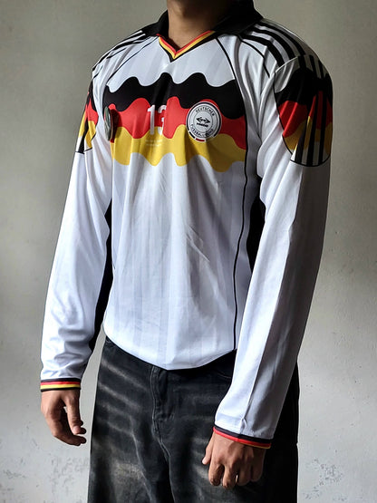 A long-sleeve Germany national football team jersey worn by a model. The jersey is white with a black collar and shoulder stripes, featuring a black, red, and yellow wavy stripe pattern across the chest and sleeves, and the DFB crest on the center chest.