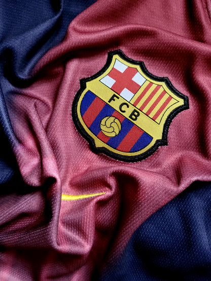 Close-up of an FC Barcelona soccer jersey fabric with the embroidered club crest centered on a draped maroon and navy background.