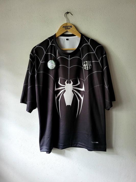 A black short-sleeve FC Barcelona soccer jersey with a white spider graphic and web pattern, hanging on a wooden hanger against a textured off-white wall.