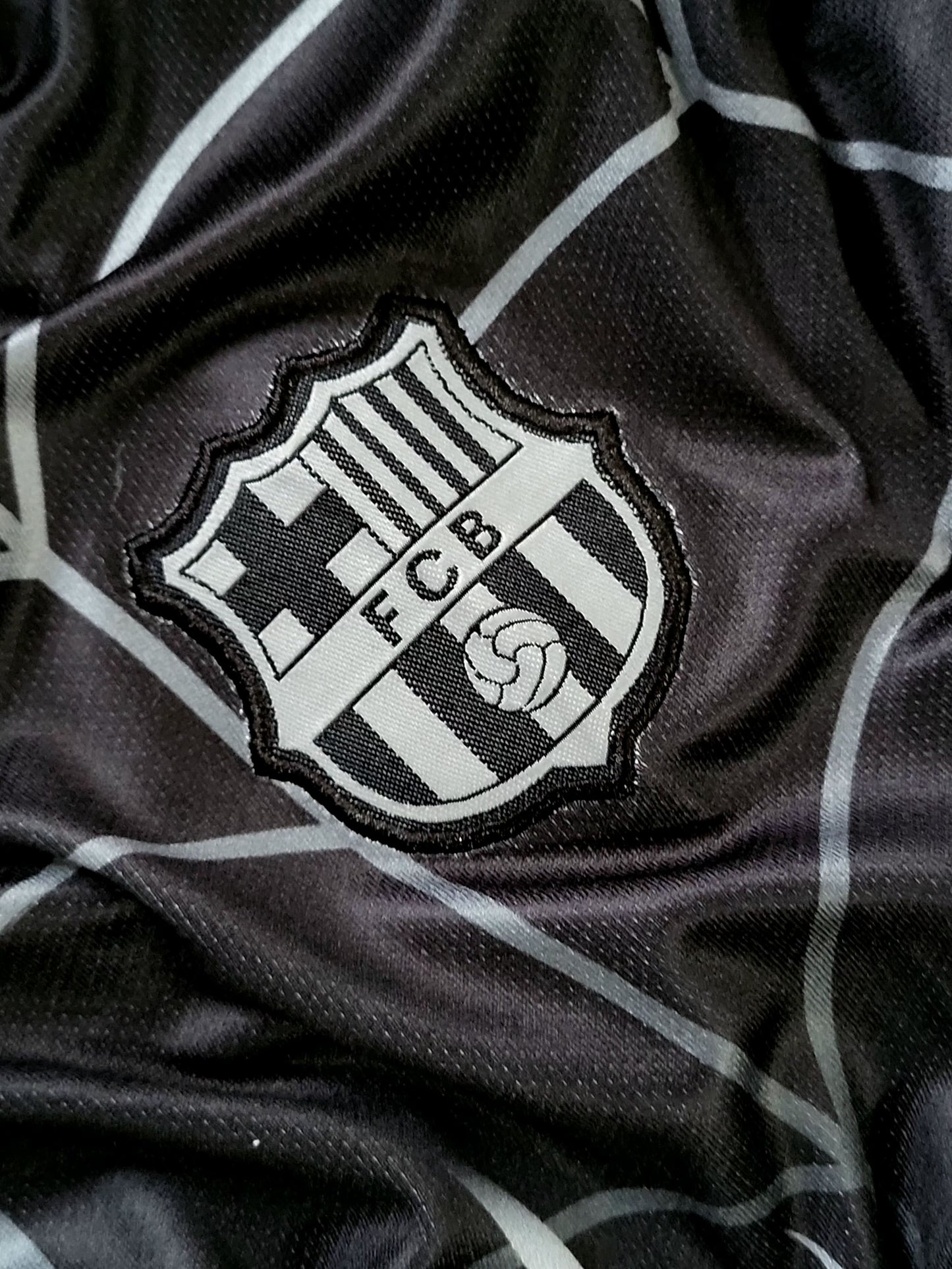 Close-up of a black and white striped soccer jersey fabric with an embroidered FC Barcelona crest patch.