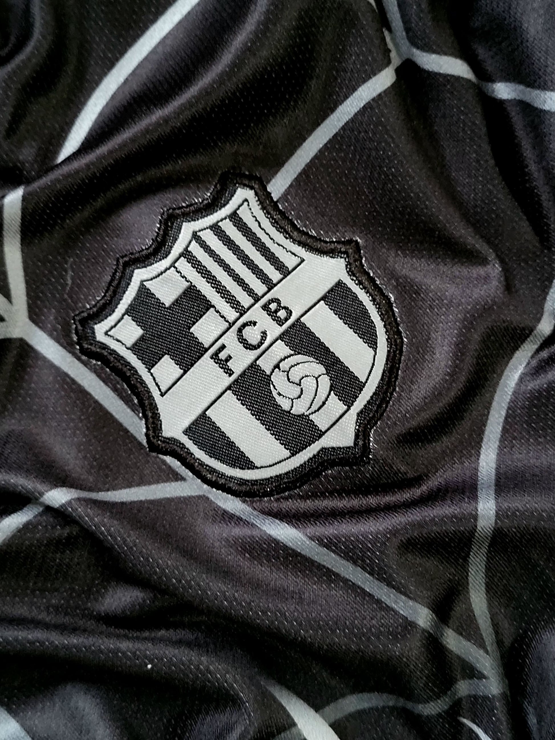 Close-up of a black and white striped soccer jersey fabric with an embroidered FC Barcelona crest patch.
