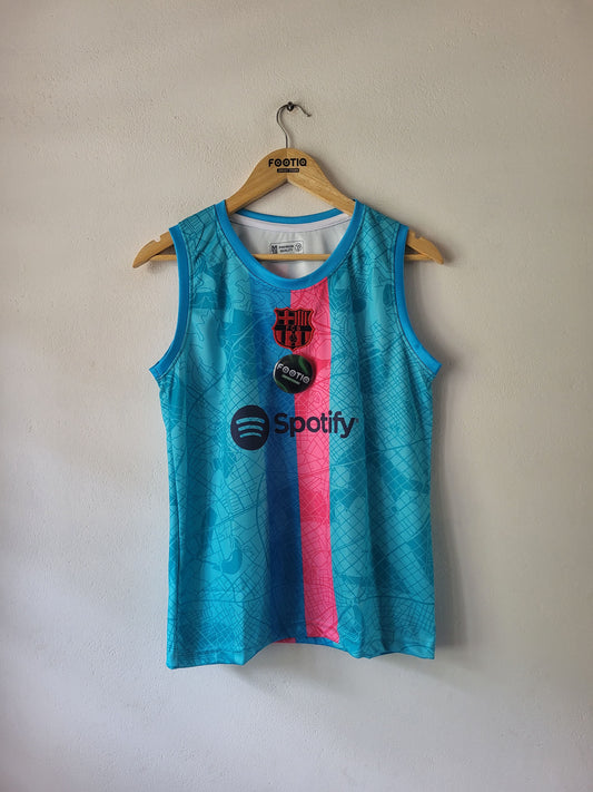 A sleeveless athletic tank top hanging on a wooden hanger against a plain beige wall. The shirt is bright turquoise blue with a vertical pink stripe down the center and black printed logos, including Spotify and FC Barcelona.