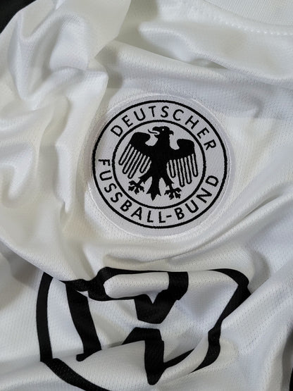 Close-up of a white soccer jersey with the circular black-and-white Deutscher Fussball-Bund crest on the chest and a large black logo below it.