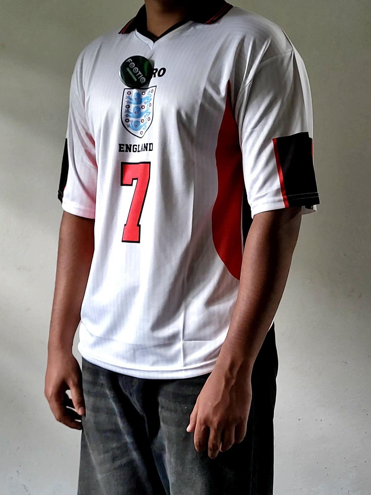 A white England soccer jersey with red and black accents, featuring the number 7 on the front, worn by a model.
