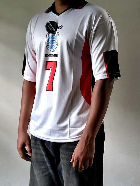 A white England soccer jersey with red and black accents, featuring the number 7 on the front, worn by a model.