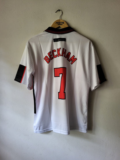 A Englans national team Beckham jersey with the name 'BECKHAM' and number '7' in red on the back, hanging on a wooden hanger against a textured wall.