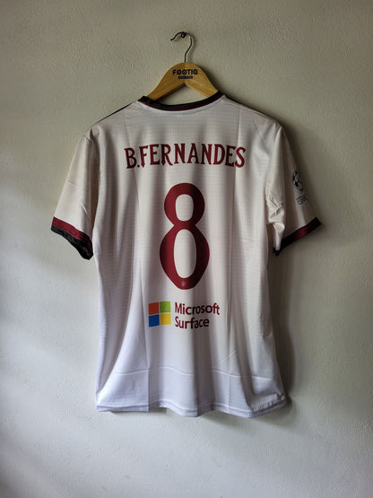 A white Manchester united soccer jersey with the back of the number 8, featuring 'B. FERNANDES' and a Microsoft Surface logo, hanging on a wooden hanger against a textured wall.