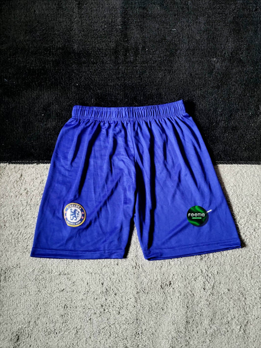 Blue Chelsea FC soccer shorts with the Chelsea crest on the left leg and a green 'FOOTGO' logo on the right leg, laid flat on a gray carpet.