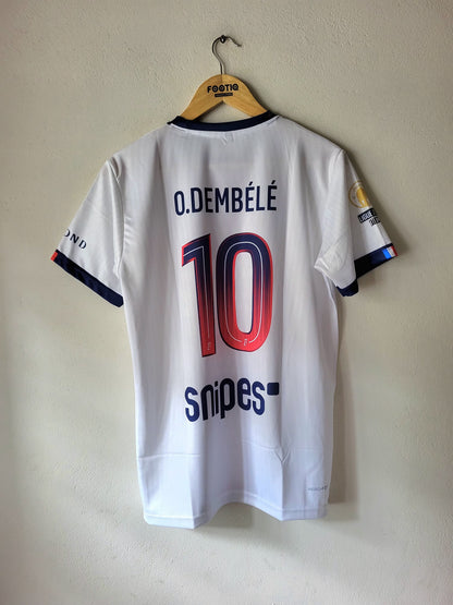 White O. Dembélé number 10 soccer jersey with navy and red accents, hanging on a wooden hanger against a beige wall.