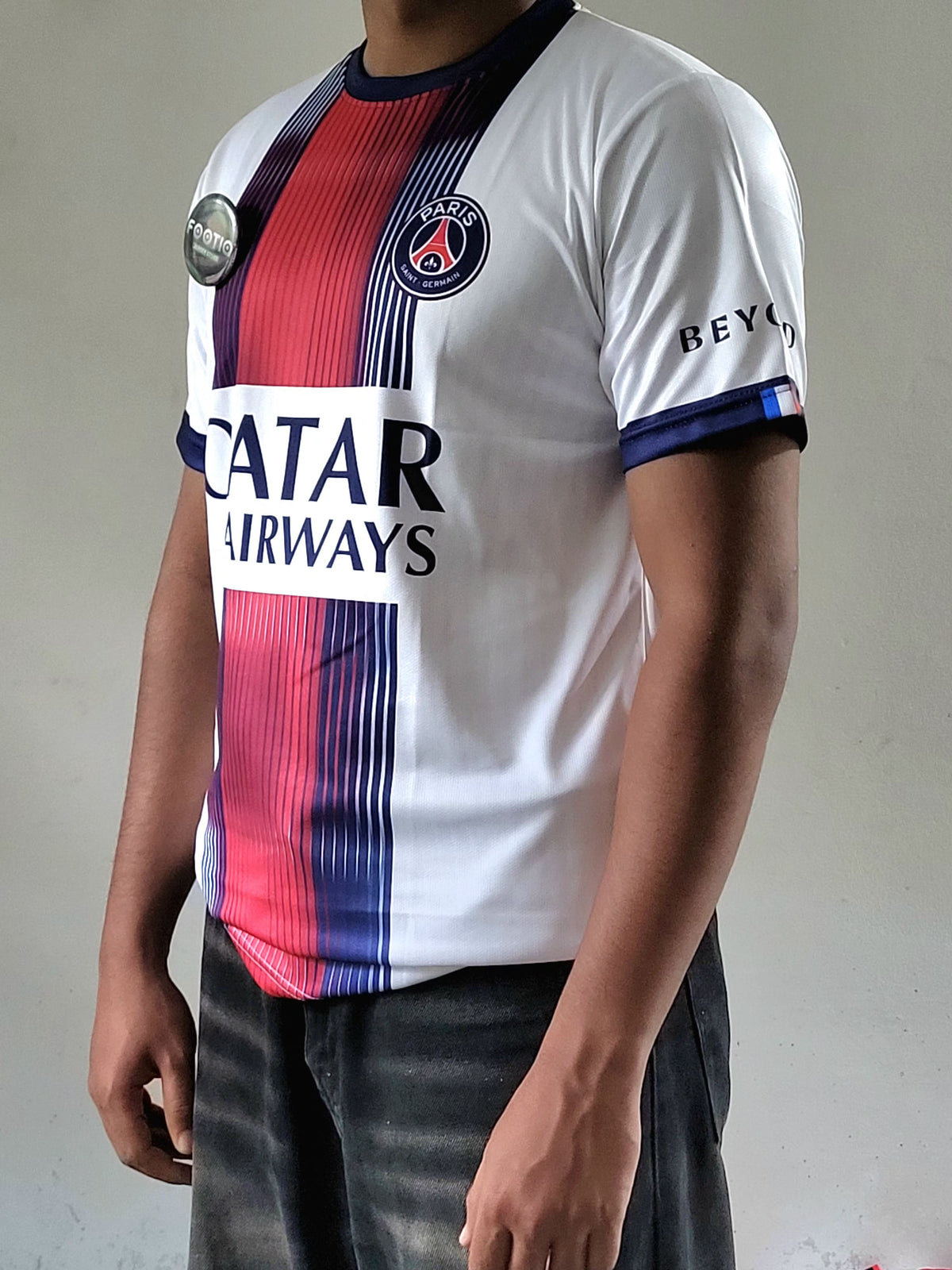 A person wearing a Paris Saint-Germain soccer jersey with a white base, red and navy blue vertical stripes, and sponsor logos including Qatar Airways and BEYTLAR.