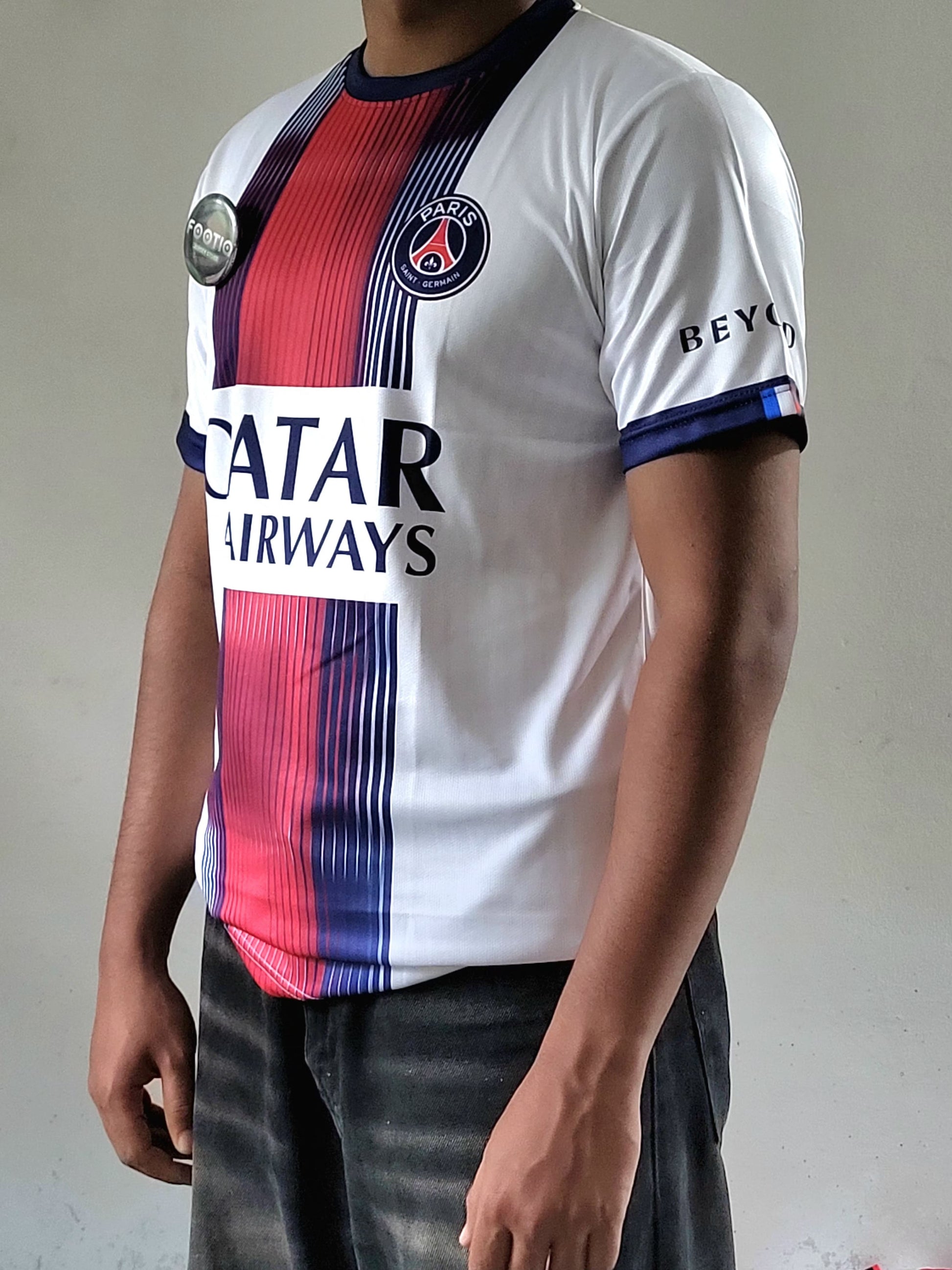 A person wearing a Paris Saint-Germain soccer jersey with a white base, red and navy blue vertical stripes, and sponsor logos including Qatar Airways and BEYTLAR.