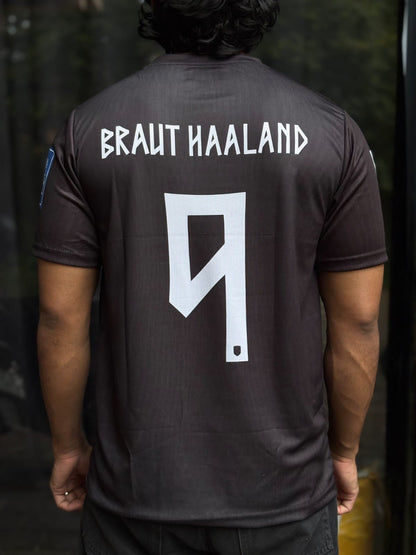 Back view of a person wearing a dark brown short-sleeve soccer jersey with 'BRAUT HAALAND' and the number 9 printed in white on the back.
