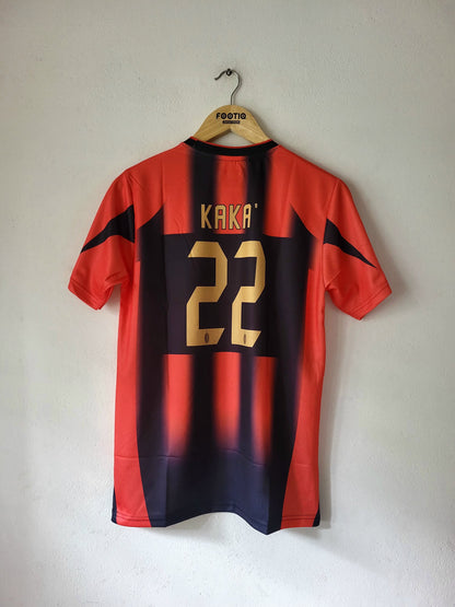 A red and navy blue striped soccer jersey with gold lettering and numbers, hanging on a wooden hanger against a plain wall. The back of the shirt features the name 'KAKA' and the number '22' in gold, and the hanger has 'FOXTROT' printed on it.