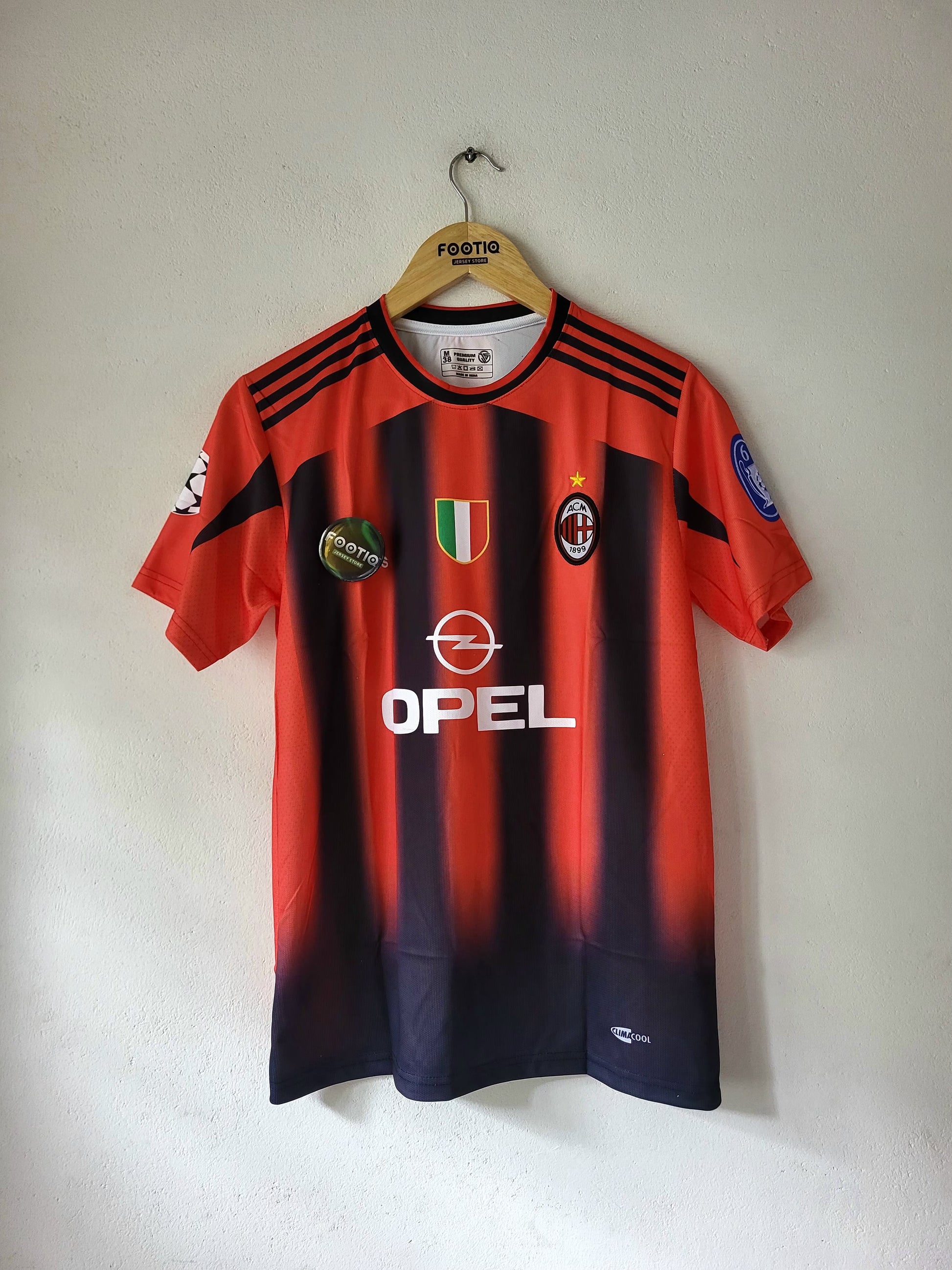 A red and navy striped AC Milan soccer jersey hanging on a wooden hanger against a plain wall. The jersey features the OPEL sponsor logo on the front, the AC Milan club crest, and the Adidas logo on the collar.