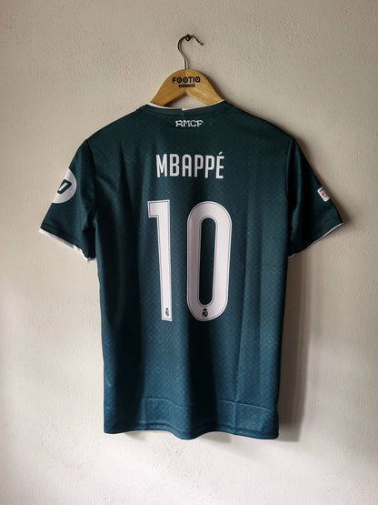 Back view of a dark teal RMC CP Mbappé jersey with the number 10 and name printed in white, hanging on a wooden hanger against a light beige wall.
