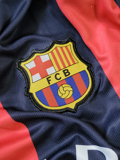 Close-up of an FC Barcelona embroidered crest patch on a navy blue athletic jersey with red side panels.