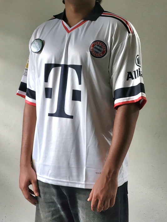 A person wearing a white Bayern Munich soccer jersey with the large T-Mobile logo on the front, black and red trim, and visible Adidas branding on the sleeve.