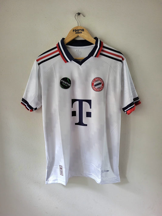 A white vintage Bayern Munich soccer jersey with the club's crest and a black Pfoerter logo, hanging on a wooden hanger against a plain beige wall.