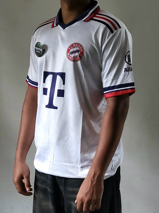 A white Bayern Munich soccer jersey with navy and red accents, featuring the club's crest and the German telecom operator T-Mobile logo, worn by a model.