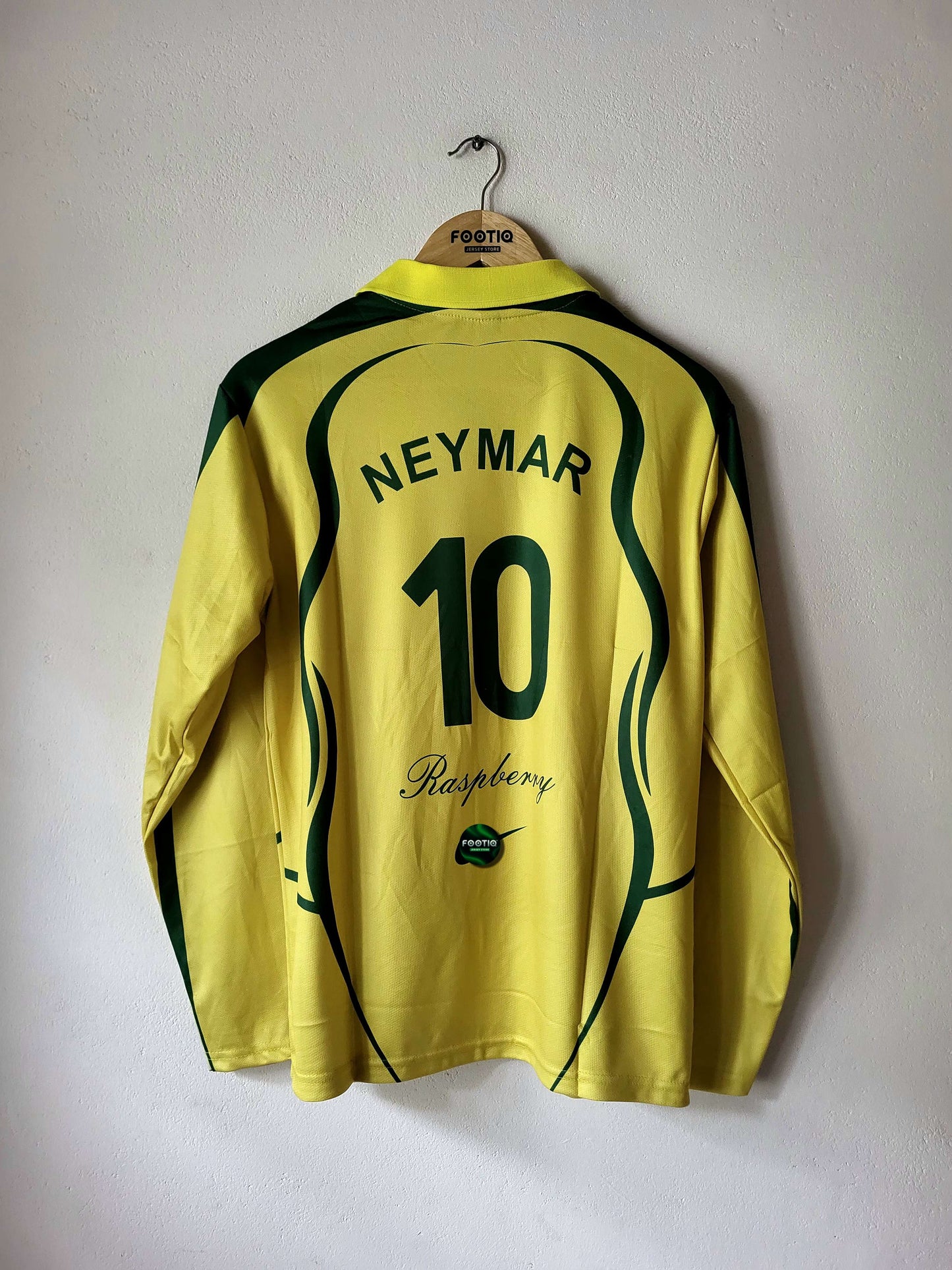 A yellow and green long-sleeve soccer jersey hanging on a wooden hanger against a plain wall. The back of the jersey features 'NEYMAR' and the number '10' in dark green, with 'Raspberry' script and a small Nike logo near the bottom.