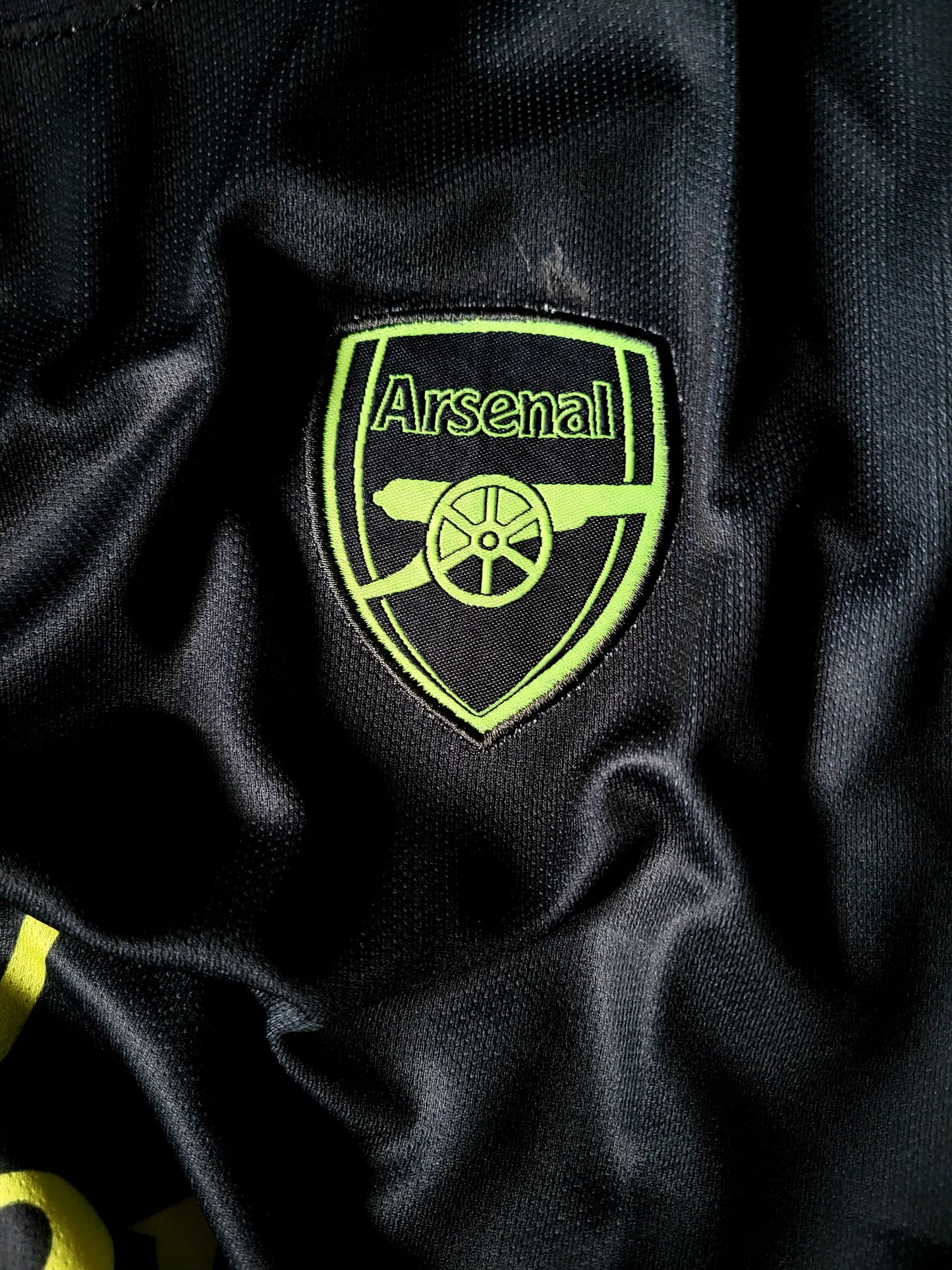 Close-up of an Arsenal football club embroidered crest patch on a black textured athletic fabric.