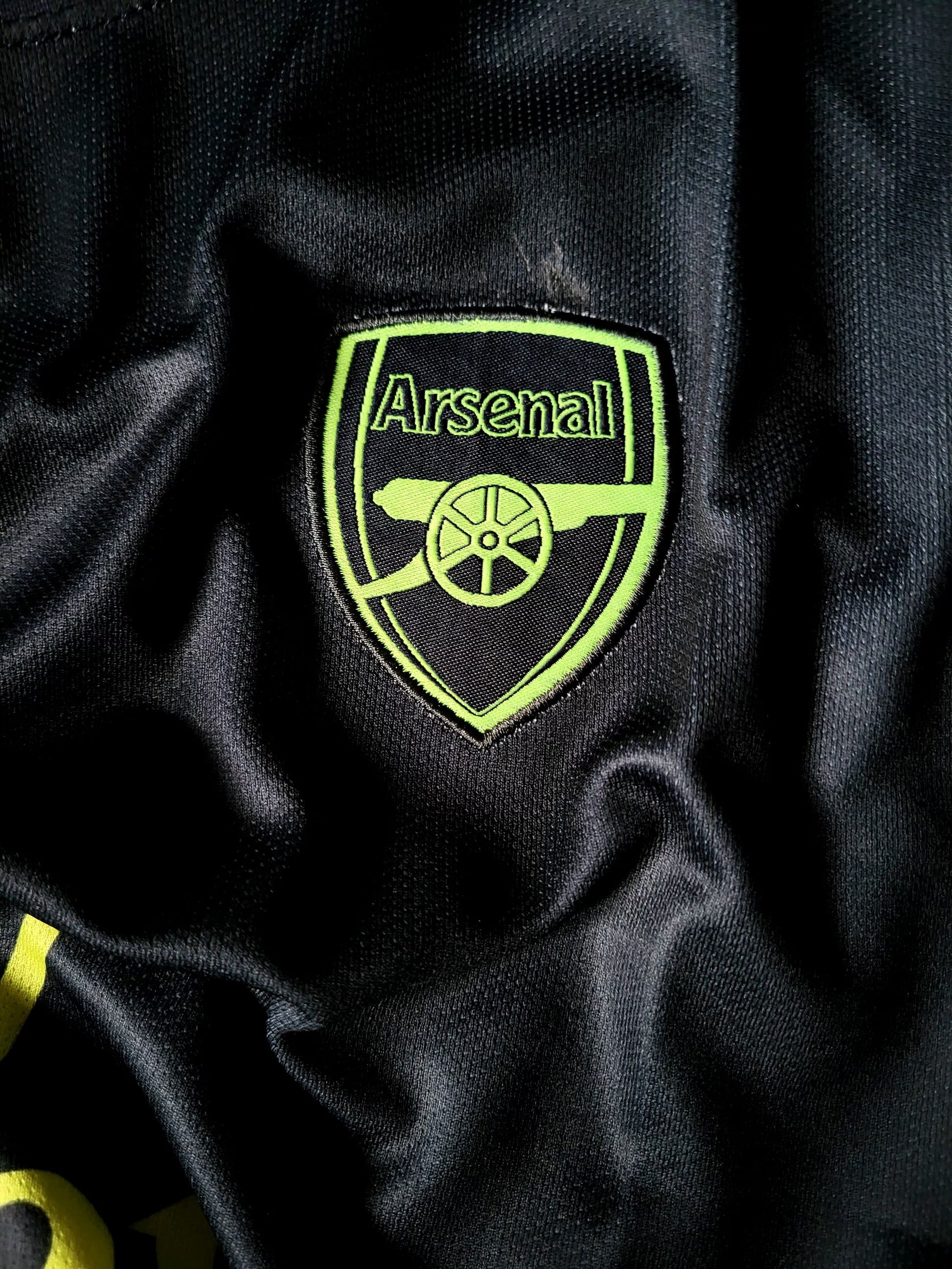 Close-up of an Arsenal football club embroidered crest patch on a black textured athletic fabric.