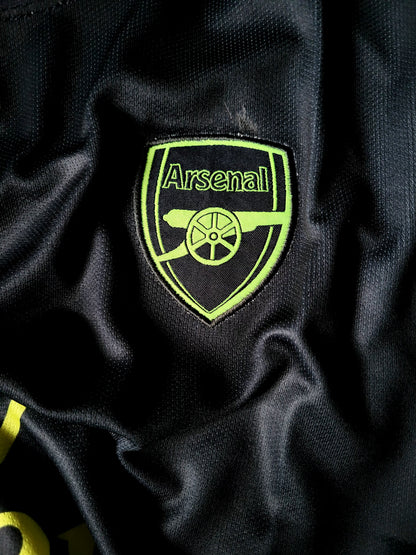 Close-up of an Arsenal football club embroidered crest patch on a black textured athletic fabric.