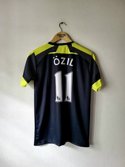 A dark navy blue soccer jersey with neon yellow-green accents on the shoulders and sleeves, featuring the name 'ÖZIL' and number '11' on the back. The jersey is hanging on a wooden hanger with 'FOOTBALL' printed on it, against a plain light gray wall.