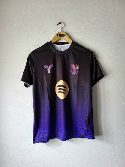 A short-sleeve FC Barcelona soccer jersey hanging on a wooden hanger against a textured white wall. The jersey features a dark gradient transitioning from black at the top to deep purple at the bottom, with a gold Spotify sponsor logo on the center chest, a purple and gold Nike Swoosh on the right chest, and the FC Barcelona crest on the left chest.
