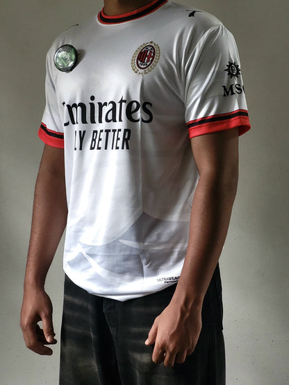 A person wearing an AC Milan soccer jersey with Emirates Fly Better branding, featuring a white body with red and black trim on the collar, cuffs, and sides.