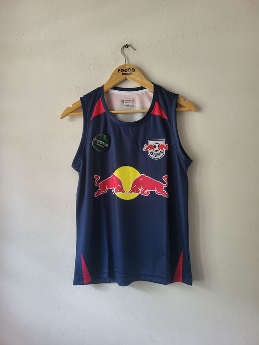 A navy blue sleeveless athletic jersey with red and yellow accents, hanging on a wooden hanger against a plain beige wall. The jersey features the Red Bull logo on the chest and a sponsor patch on the right side.