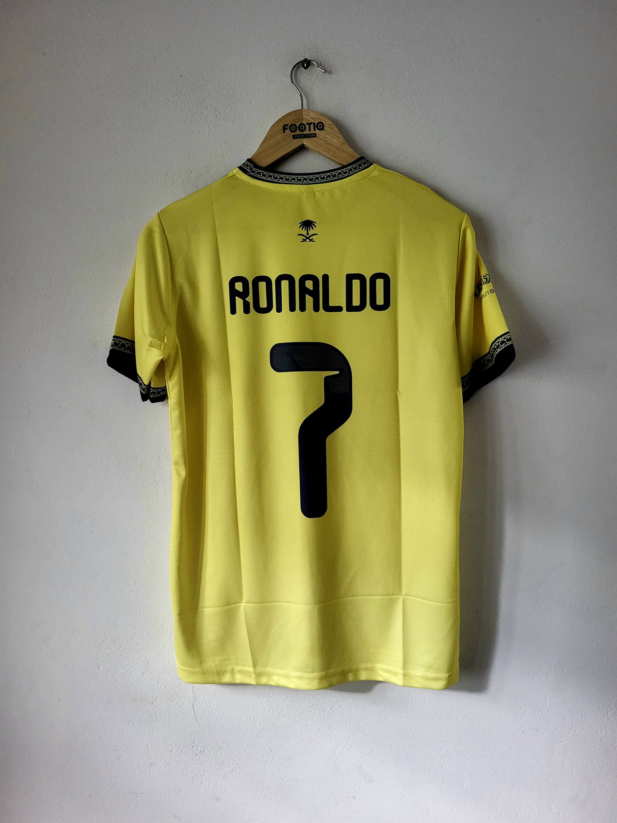 A yellow soccer jersey with 'RONALDO' and the number '7' printed in black on the back, hanging on a wooden hanger against a plain light gray wall.