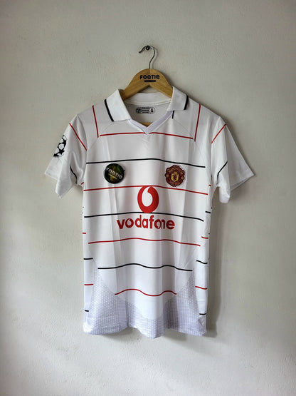 A vintage white Manchester United football shirt with red and black stripes, featuring the red Vodafone logo and club crest, hanging on a wooden hanger against a plain wall.