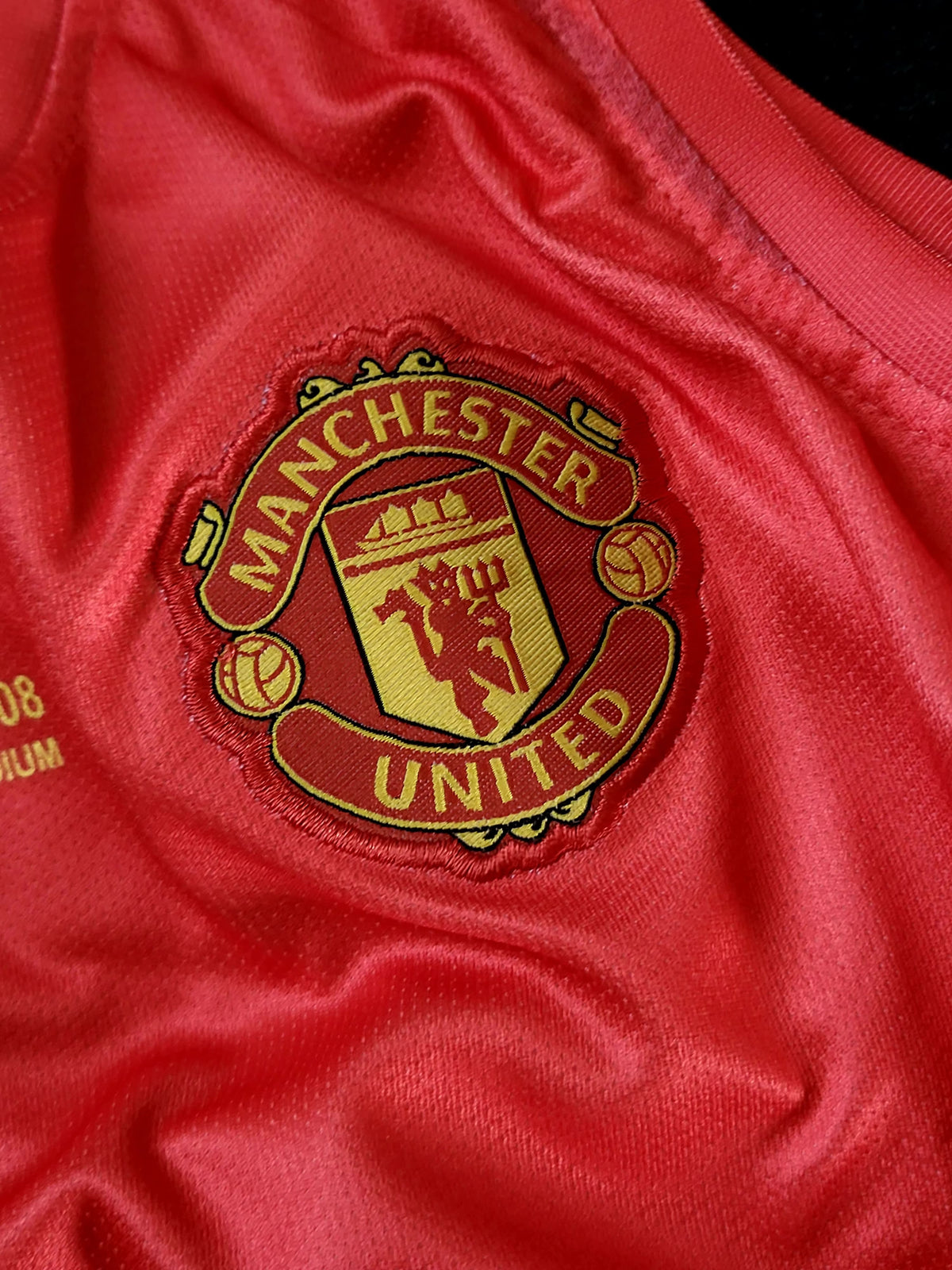 Close-up of a red Manchester United soccer jersey fabric with the embroidered club crest in gold and red.