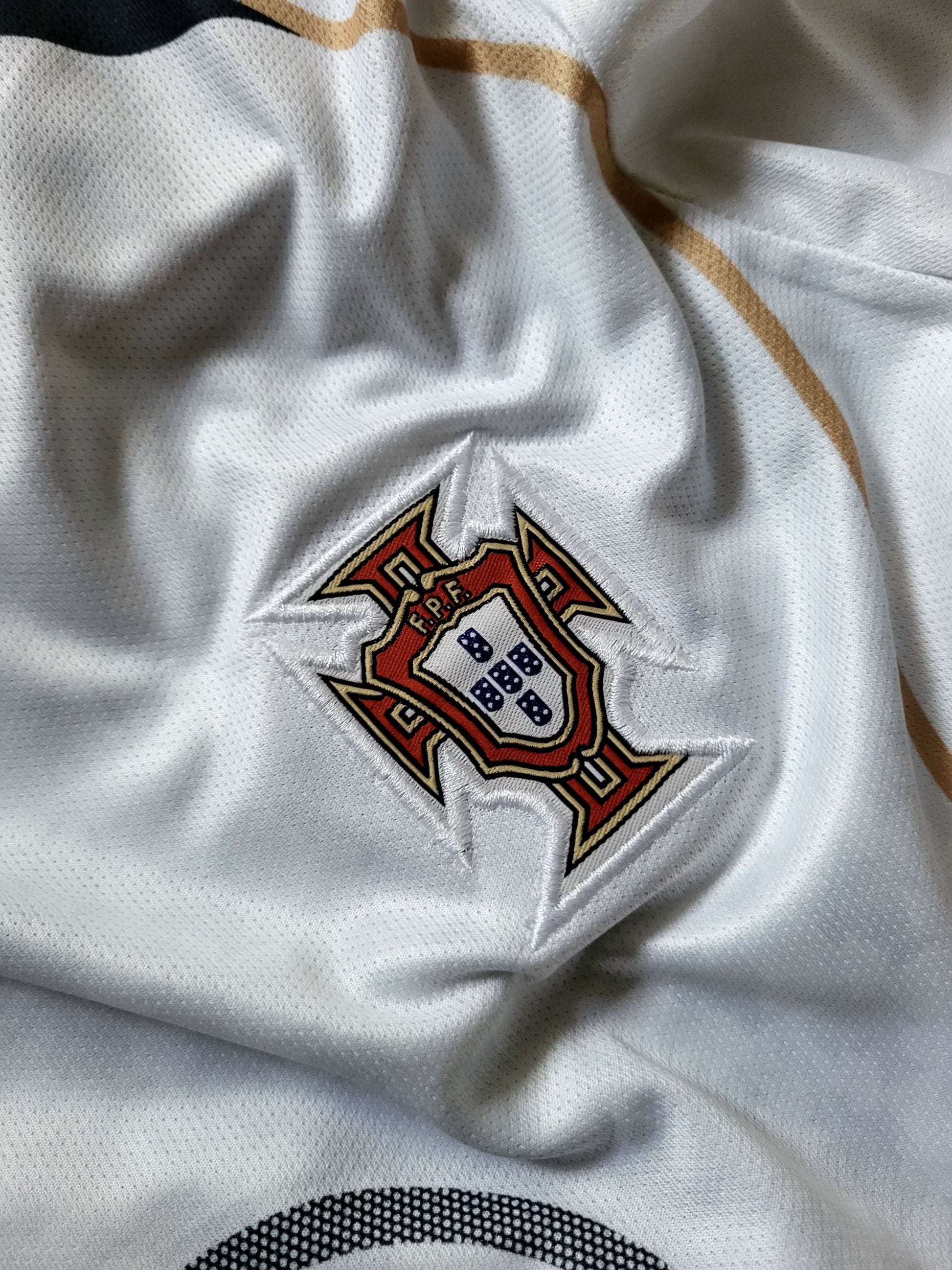 Close-up of a white Portugal soccer jersey fabric showing the embroidered national team crest on the chest.
