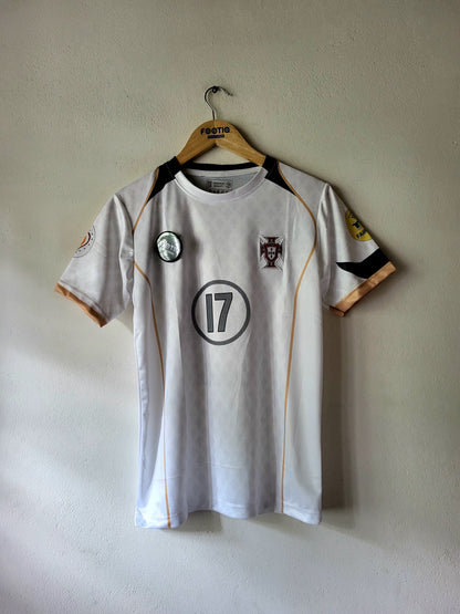 A white Portugal soccer jersey with black and gold accents, featuring the number 17 on the chest, hanging on a wooden hanger against a textured beige wall.