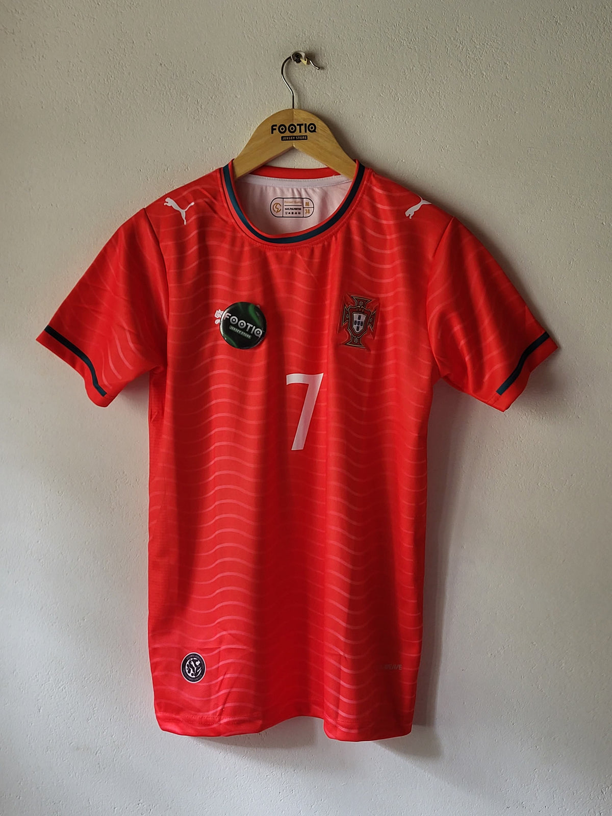 A red Puma soccer jersey with black and white accents, featuring the number 7 on the front, laid flat on a light beige wall.
