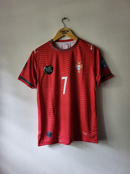 A red Portugal soccer jersey with the number 7 on the front, hanging on a wooden hanger against a textured off-white wall.